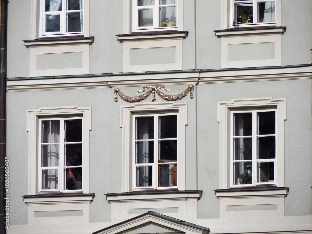 Fototapeta premium Close-up of a light-gray historic building facade with ornate stucco elements and three large rectangular windows in Warsaw Old Town.
