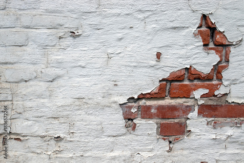 A fragment  of a brick wall painted white. Some of the plaster has peeled off, revealing the red brickwork. The brick wall is painted white.