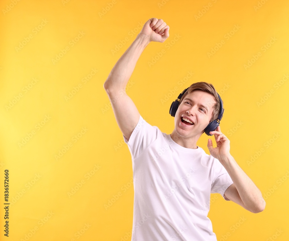 Fototapeta premium Man with headphones listening to music and dancing on yellow background