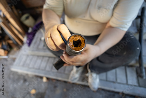 A man holds a section of an old water pipe with visible traces of rust and mineral deposits that reduce the internal diameter and impede water flow An old water pipe with limescale and rust deposits.