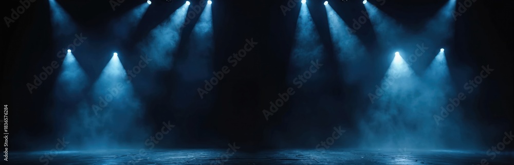 Fototapeta premium Stage lights illuminate dark space with blue beams piercing through smoke. Empty theater floor awaits performers, creating dramatic atmosphere for shows.