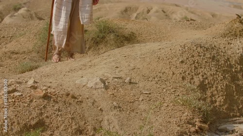 Sandaled feet move slowly across the arid terrain. Christian and spiritual concept. Slow motion shot