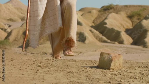 A wanderer in ancient-style clothing stepping across a dusty desert path. Christian and spiritual concept. Slow motion Shot