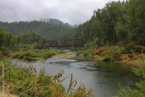 photo of railroad bridge crossing a river in the forest during a rainstorm with rain drops falling on the stream