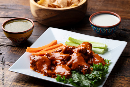 Canvas Print Chicken wings and drums in a red sauce on a white plate with carrots, celery, le