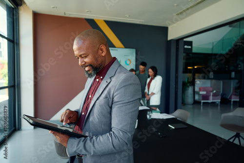 Side view of black mature businessman using tablet in meeting room at workplace