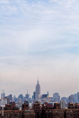Empire State Building and midtown Manhattan skyline seen from the Brooklyn Bridge, featuring urban architecture and the iconic New York City cityscape under a bright sky
