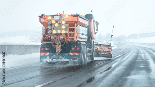 Snow plow sprinkles highway with road salt in freezing weather.