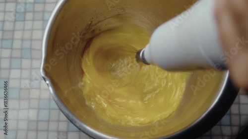 Top view, elderly woman's hand beating eggs with kitchen mixer in metal bowl