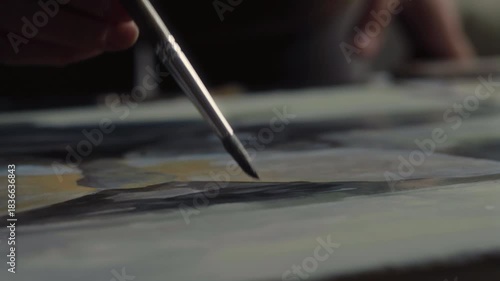 Close-up, the artist's hand paints a painting with a brush on a table in her studio