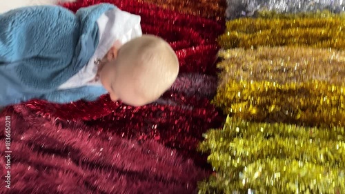 Little child touching multicoloured tinsel. Christmas holidays content. 4K vertical footage.