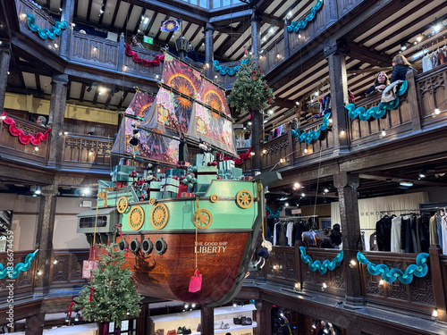 London, UK, A festive “Good Ship Liberty” installation loaded with wrapped gifts, suspended in the wooden-balconied atrium of Liberty London, decorated with garlands and watched by shoppers.
