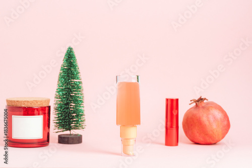 Holiday-themed beauty products with candle, miniature tree, cosmetic bottle and pomegranate on pink background