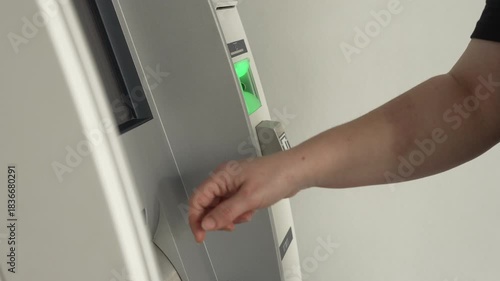 Hand touching ATM touchscreen at banking terminal as person selects options on screen near green card slot for electronic payment and cash withdrawal concept