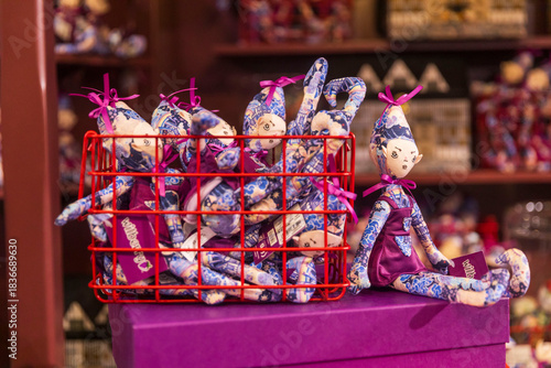 London, UK, 6 December 2025, A close-up of Liberty London’s Christmas dolls, showing small rag dolls in blue floral fabric displayed in a red wire basket on a purple box.