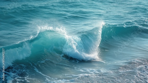 Waves roll onto the sandy beach during the day. The water glimmers under the sunlight as the waves crash and create splashes. The scene captures the movement of the ocean.