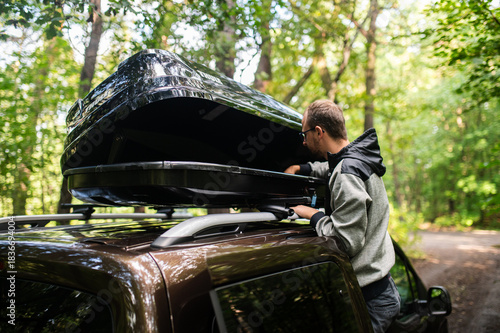 Man Attaching or Opening a Black Roof Box on a Car in the Forest