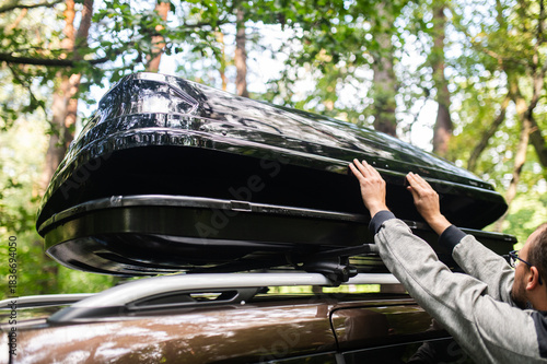 Man Attaching or Opening a Black Roof Box on a Car in the Forest