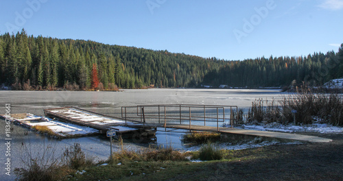 photo of ice on Elk River Reservoir in Idaho mountains with a background of trees and forest and foreground with a fishing dock