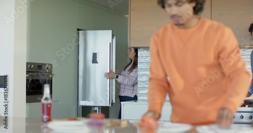 Friends meeting in kitchen slicing tomatoes grabbing cheese stirring and arranging buns for burgers