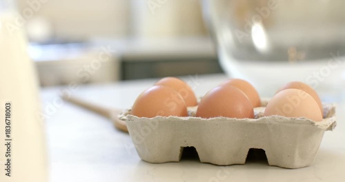 Camera is shifting focus to eggs and spoon near mixing bowl on countertop for baking prep