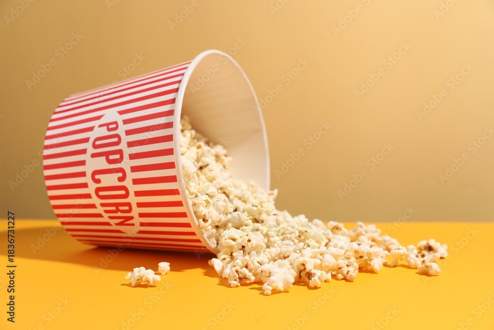 Obraz premium Tasty popcorn in paper cup on orange table against beige background, closeup