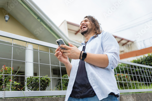 LGBTQ man laughing while using smartphone outdoors