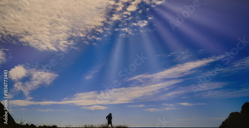 Silhouette hiker on a hilltop under dramatic sun rays in a wide blue sky