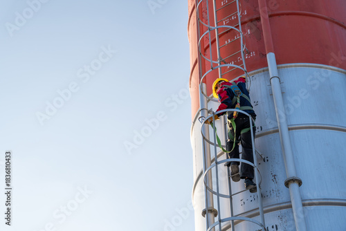 Fotografie a worker climbing the fixed ladder of a tall cement silo, emphasizing industrial height and safety