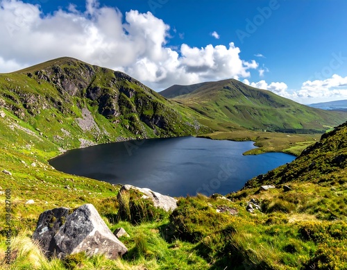 Scenic overview of a mountain lake with surrounding green hills, under a blue sky