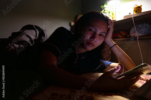 Thai Girl wearing pajamas uses phone on bed