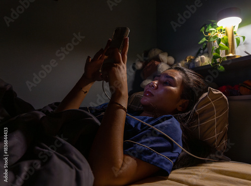 Thai Girl wearing pajamas uses phone on bed