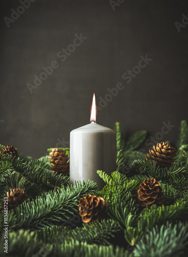 Festive glow: A candle among fir branches and cones. Cozy winter mood. Selective focus.