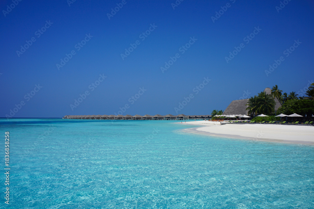 Fototapeta premium Overwater Bungalows and White Sand Beach in the Shallow Turquoise Sea of Maldives