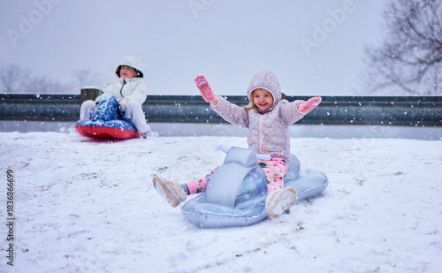 Joyful Children Sledding Down a Snowy Hill – Winter Fun and Laughter on Inflatable Sleds. Winter Thrill Ride