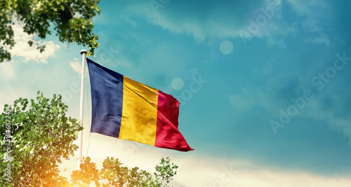 Chad national flag waving in the sky behind the tree. The flag blowing with beautiful sunlight. Chad national flag for independence day.