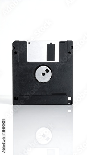 Close-up studio shot of a black square floppy disk, silver spindle, and white protection slide, reflecting on the surface below