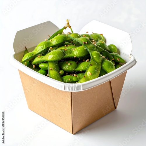 Close-up studio shot of a brown paper container filled with vibrant green pods. The snack is sprinkled with sesame seeds