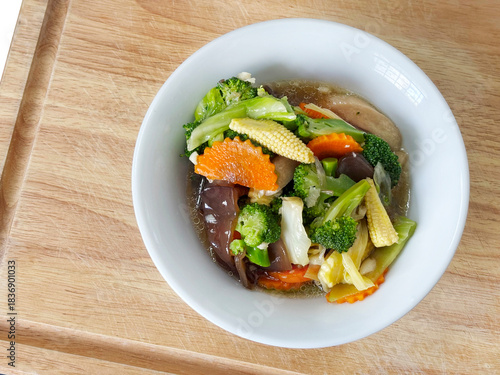 Colorful stir-fried mixed vegetables in oyster sauce, featuring broccoli, carrots, baby corn, and mushrooms, served in a white bowl on a wooden tray, fresh healthy plant-based cuisine