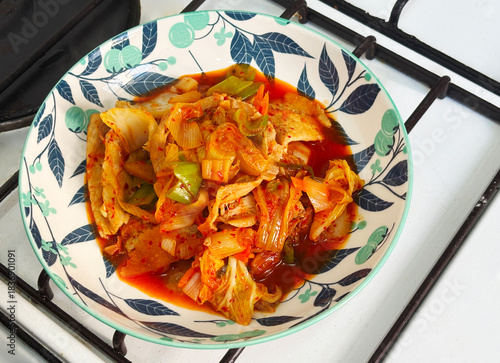 Vibrant stir-fried sliced pork with spicy kimchi, served in a decorative bowl with floral patterns. This dish showcases a blend of colors and textures, perfect for food photography