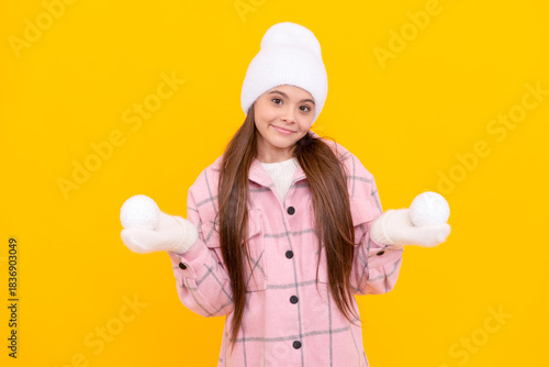 happy child in hat and mittens playing snowballs on yellow background, fun
