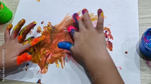 Children's hands smear bright finger paints on a piece of paper, creating an abstract drawing and developing creativity.
