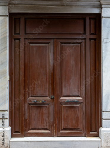 Classic wooden double door with decorative panels and vintage handles, framed by marble walls, showcasing traditional architecture and elegant historic craftsmanship.