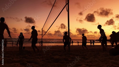 Young people playing beach volleyball by the ocean at sunset