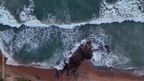 Giant ocean waves crashing and foaming on empty sand tropical beach with big rock stones