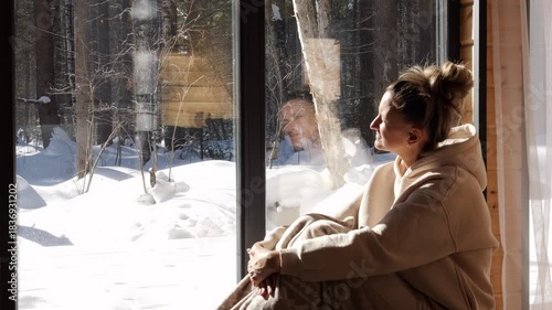 Woman wrapped in blanket enjoys quiet warmth peaceful mind near window facing forest Morning light fills cabin as forest reflects calm balance deep forest presence enhances mindful serene of peace