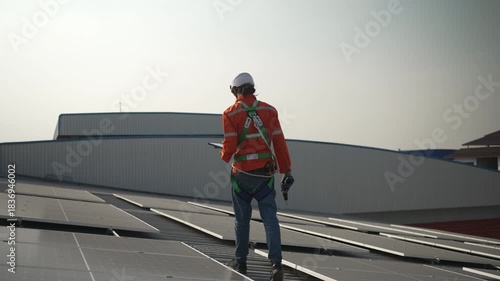 Blue collar worker is inspecting solar panel at rooftop of factory. Energy, sustainability.
