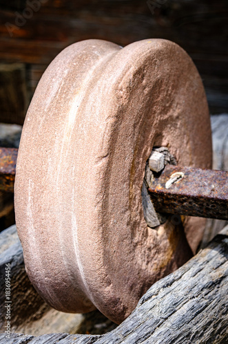 Historical stone wheel used for grinding grains in a rustic farming setting during daylight hours in an outdoor environment