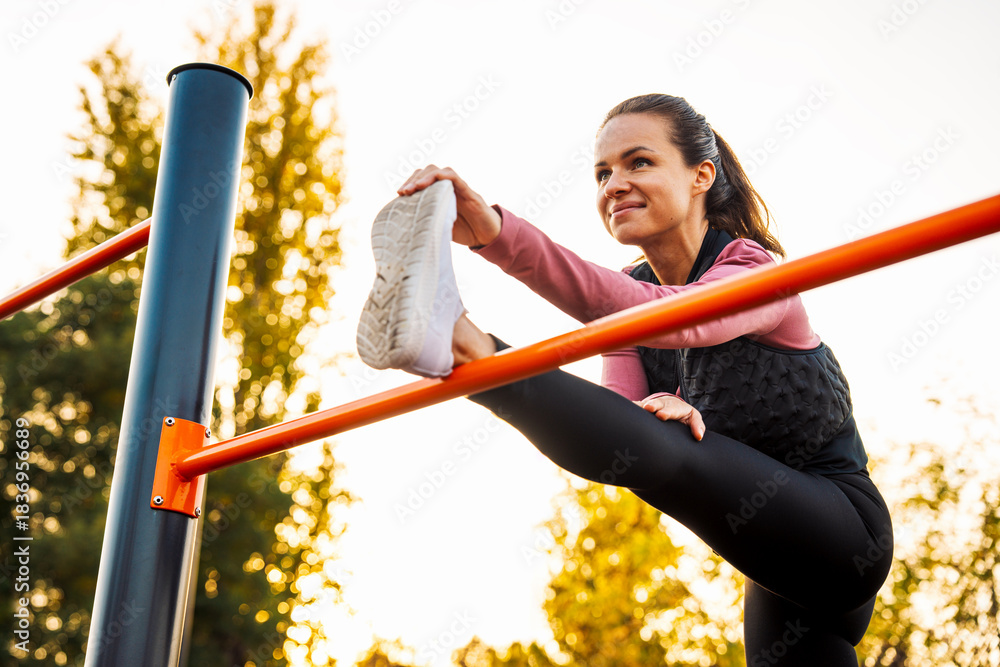 Fototapeta premium Smiling woman doing warm up stretching exercise outdoors.