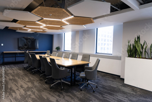 Long wooden conference table is anchoring office meeting room with gray chairs and honeycomb panels